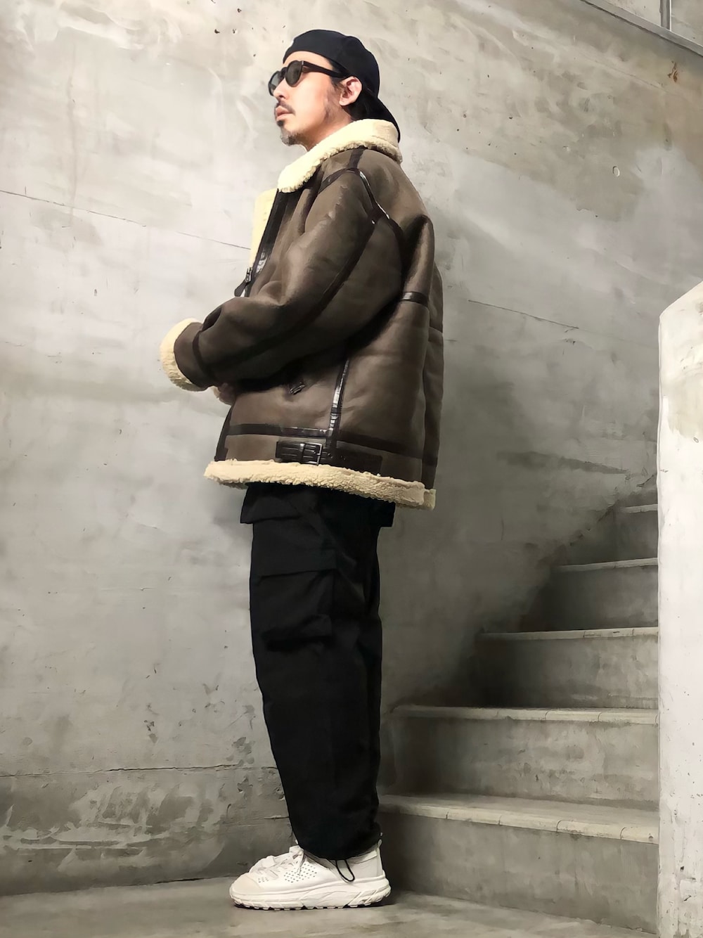 ブラック系のカーゴパンツ、ブラウン系のムートンコート、ブラック系のサングラスを着用したメンズの冬コーディネートの1枚目の写真