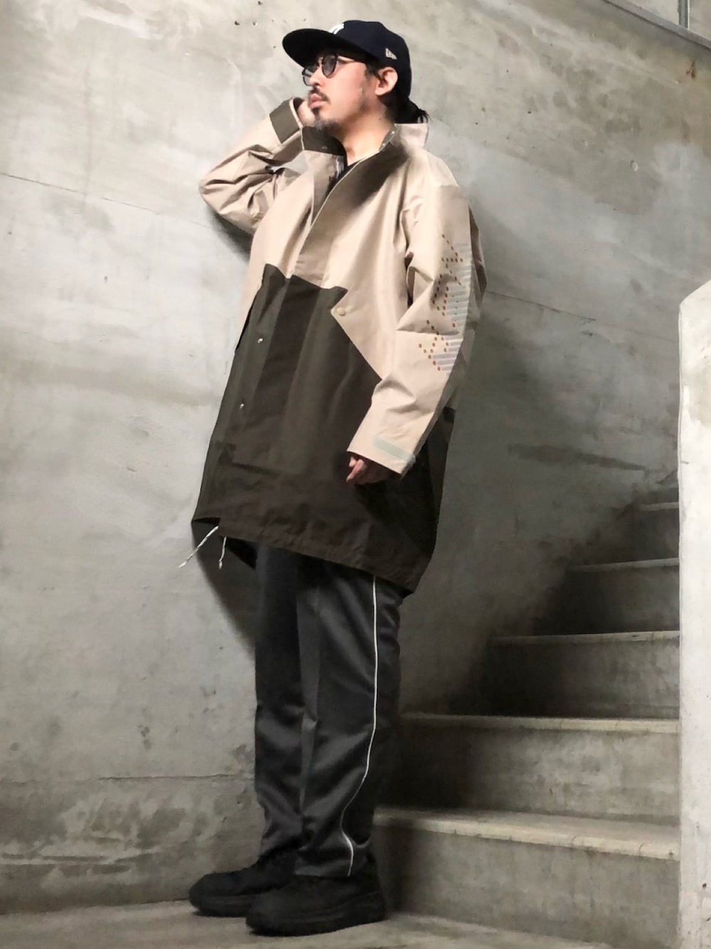 ベージュ系のナイロンジャケット、グレー系のその他パンツ、ブラック系のキャップを着用したメンズの春コーディネートの1枚目の写真