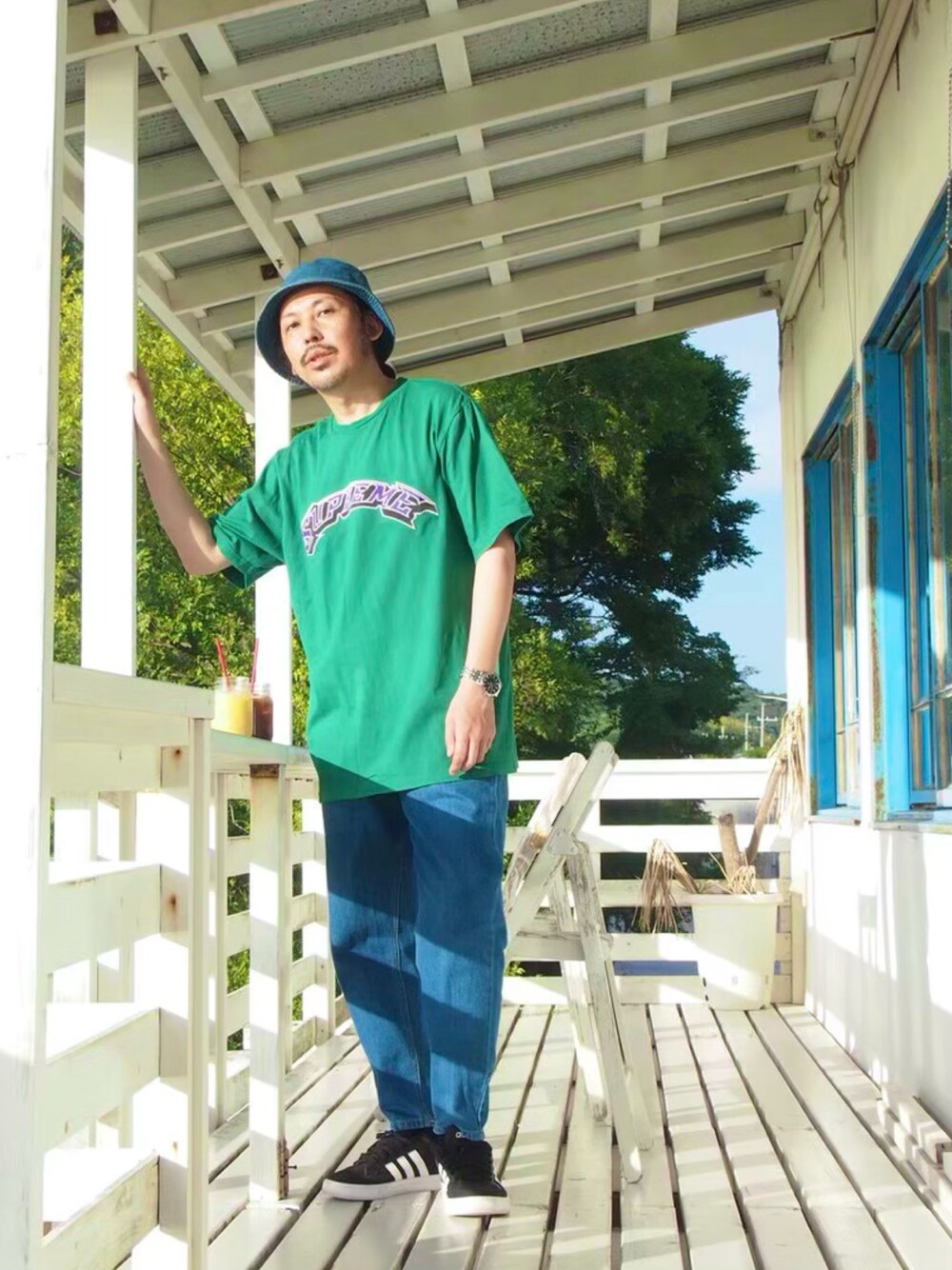 ブラック系のスニーカー、グリーン系のTシャツ/カットソー、ブルー系のハットを着用したメンズの春コーディネートの1枚目の写真