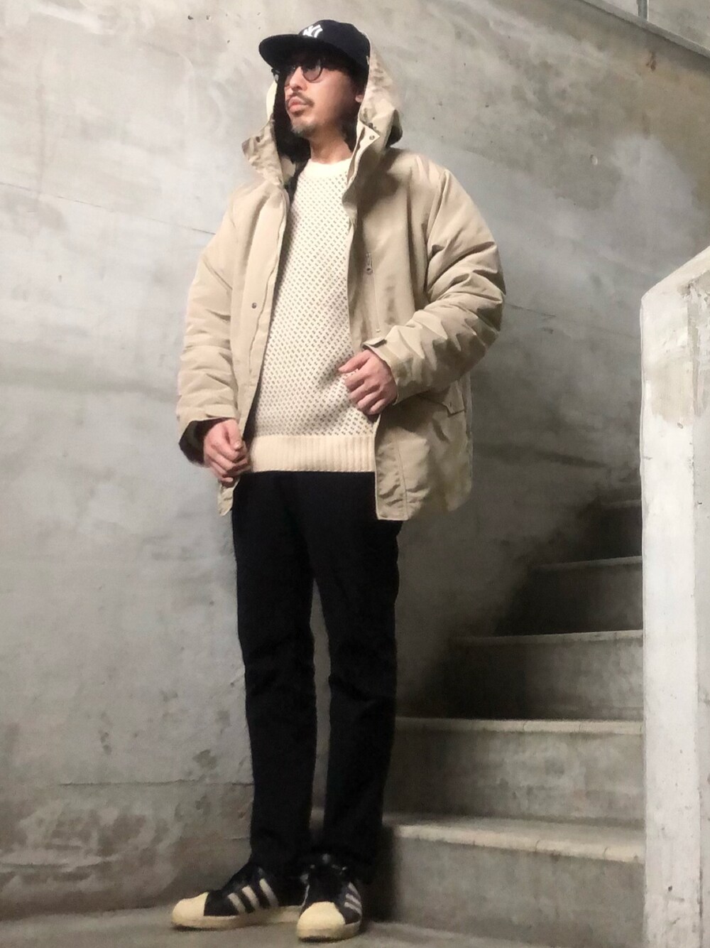 ベージュ系のマウンテンパーカー、ホワイト系のニット/セーター、ブラック系のチノパンツを着用したメンズの冬コーディネートの1枚目の写真