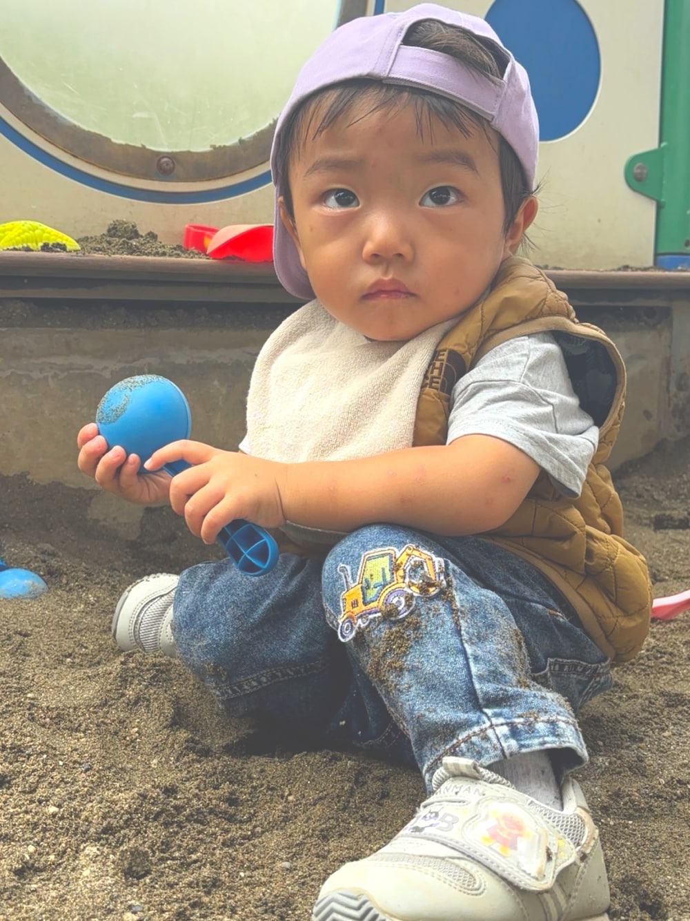 ベージュ系のベスト、グレー系のスニーカー、パープル系のキャップを着用したキッズの秋コーディネートの1枚目の写真