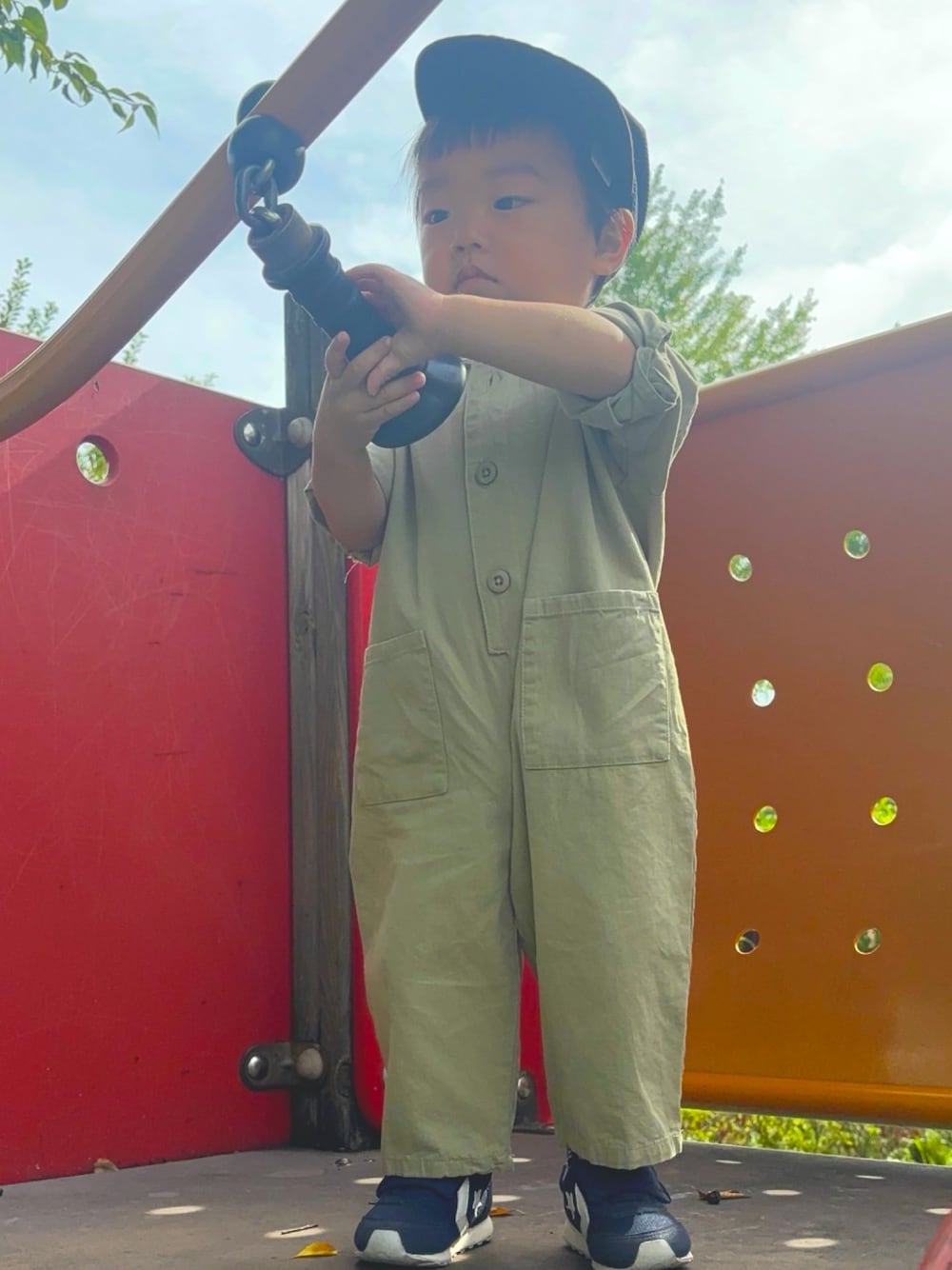 グリーン系のオールインワン・サロペット、ホワイト系のスニーカー、ブラック系のキャップを着用したキッズの秋コーディネートの1枚目の写真