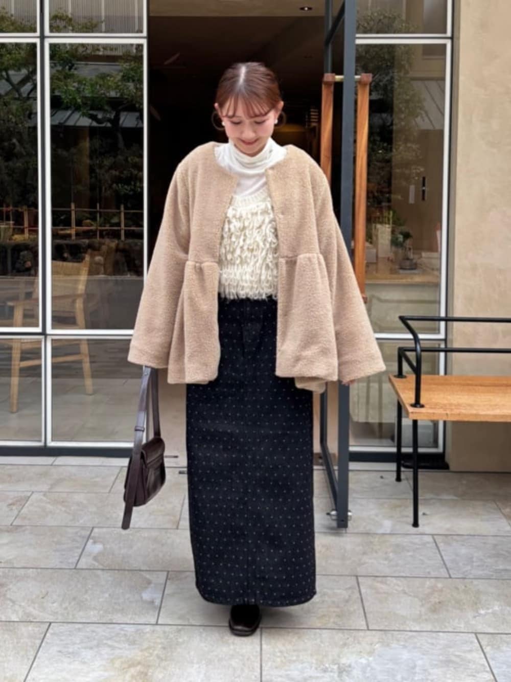 ホワイト系のベスト、ブラック系のデニムスカート、ベージュ系のノーカラーコートを着用したレディースの冬コーディネートの1枚目の写真