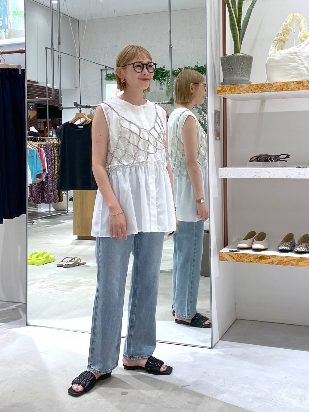 シルバー系のベスト、ホワイト系のタンクトップ、ブルー系のデニムパンツを着用したレディースの夏コーディネートの1枚目の写真