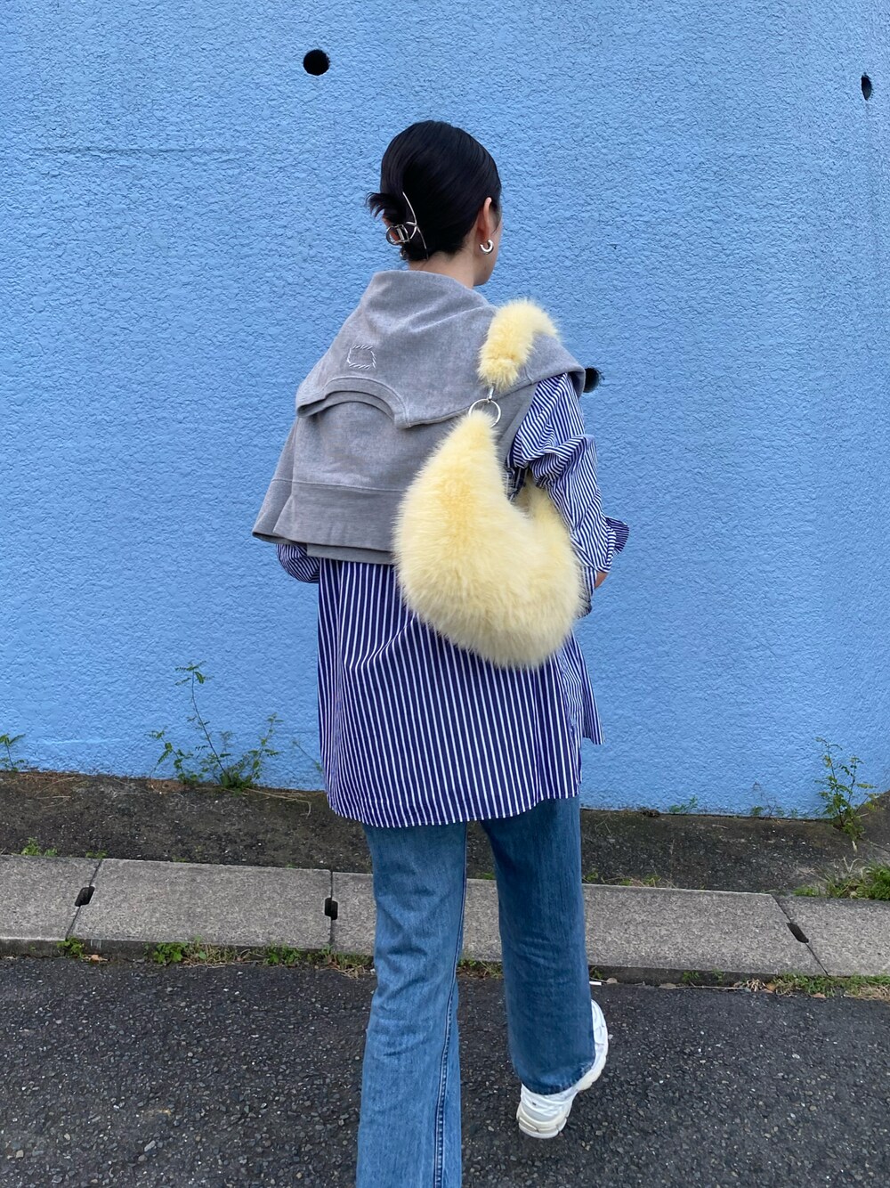 イエロー系のハンドバッグ、ブルー系のデニムパンツ、ホワイト系のスニーカーを着用したレディースの秋コーディネートの1枚目の写真