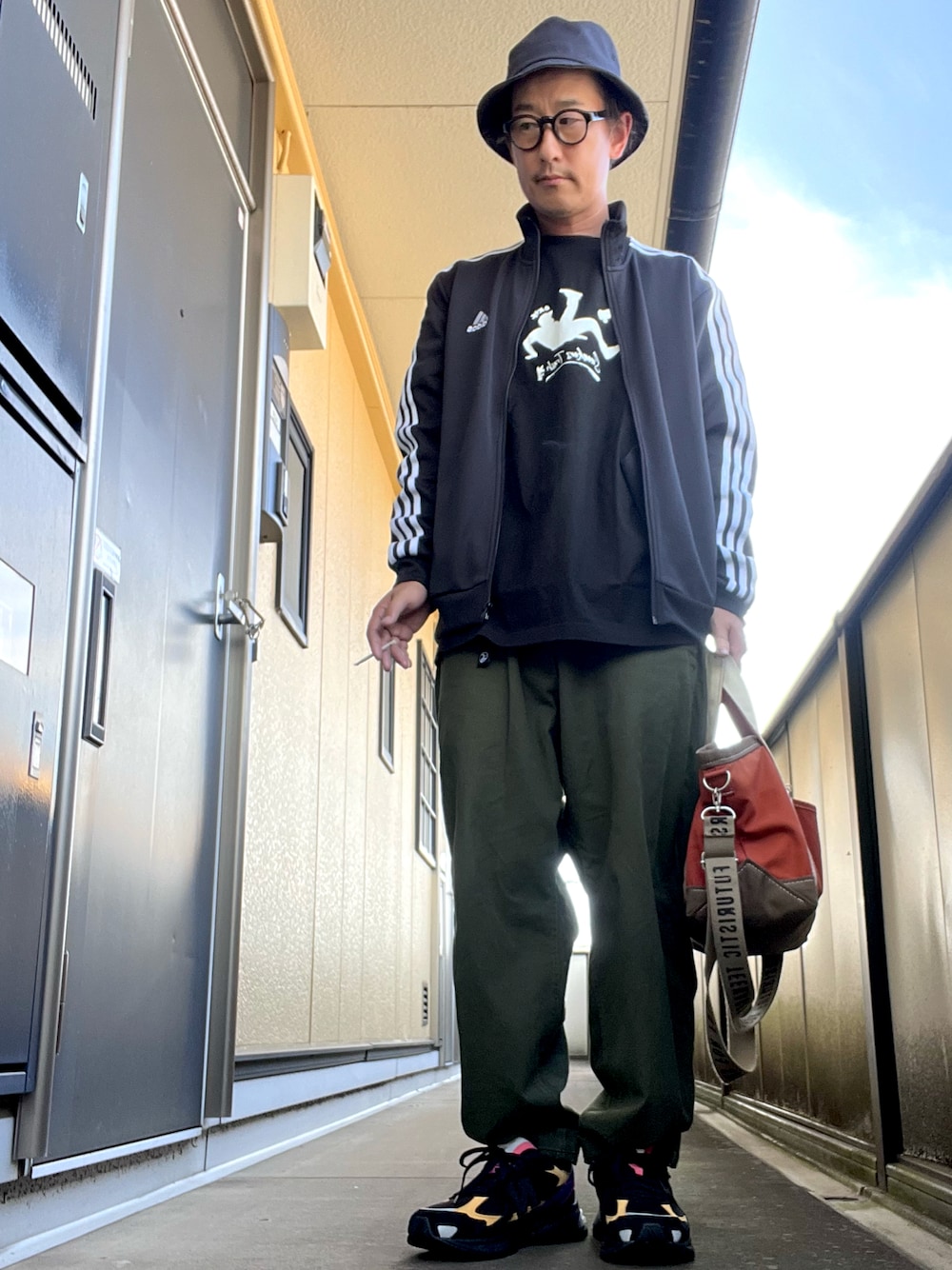 オレンジ系のトートバッグ、ブラック系のTシャツ/カットソー、グリーン系のチノパンツを着用したメンズの秋コーディネートの1枚目の写真