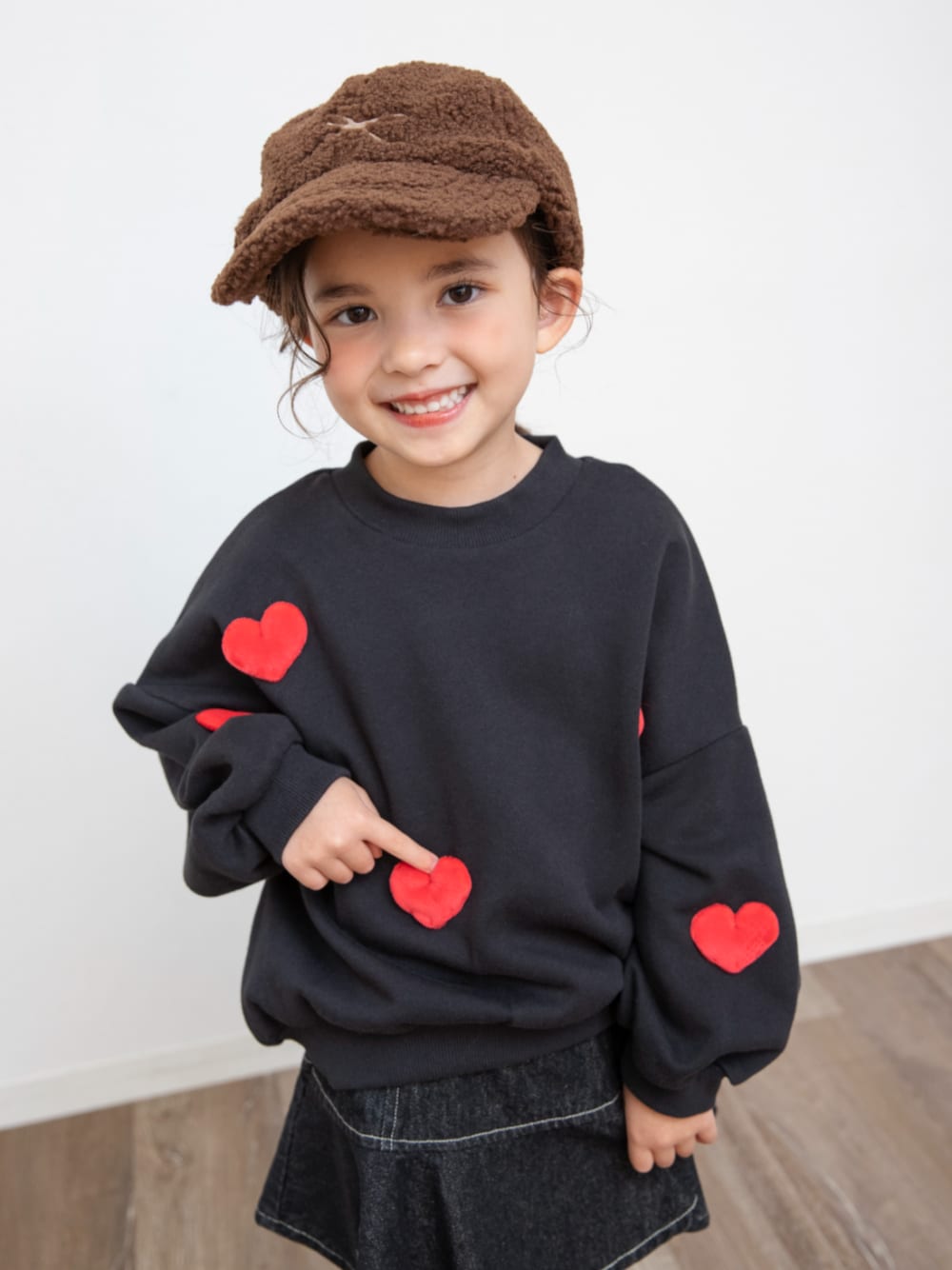 ブラック系のスウェット、ブラック系のデニムスカート、ブラウン系のキャップを着用したキッズの冬コーディネートの1枚目の写真