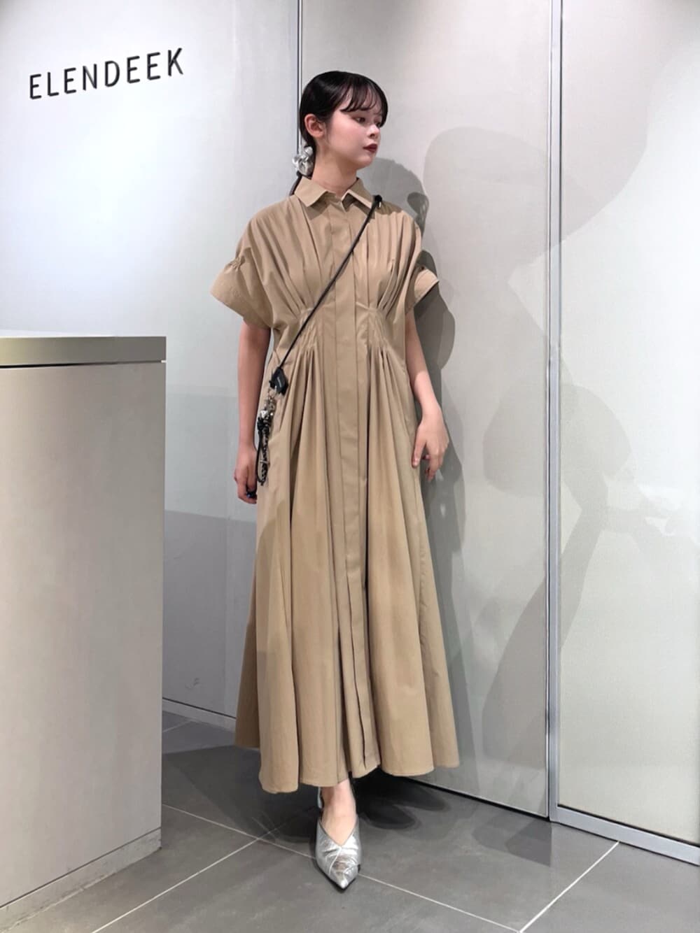 シルバー系のパンプス、ベージュ系のワンピース、ブラック系のスマホグッズを着用したレディースの夏コーディネートの1枚目の写真