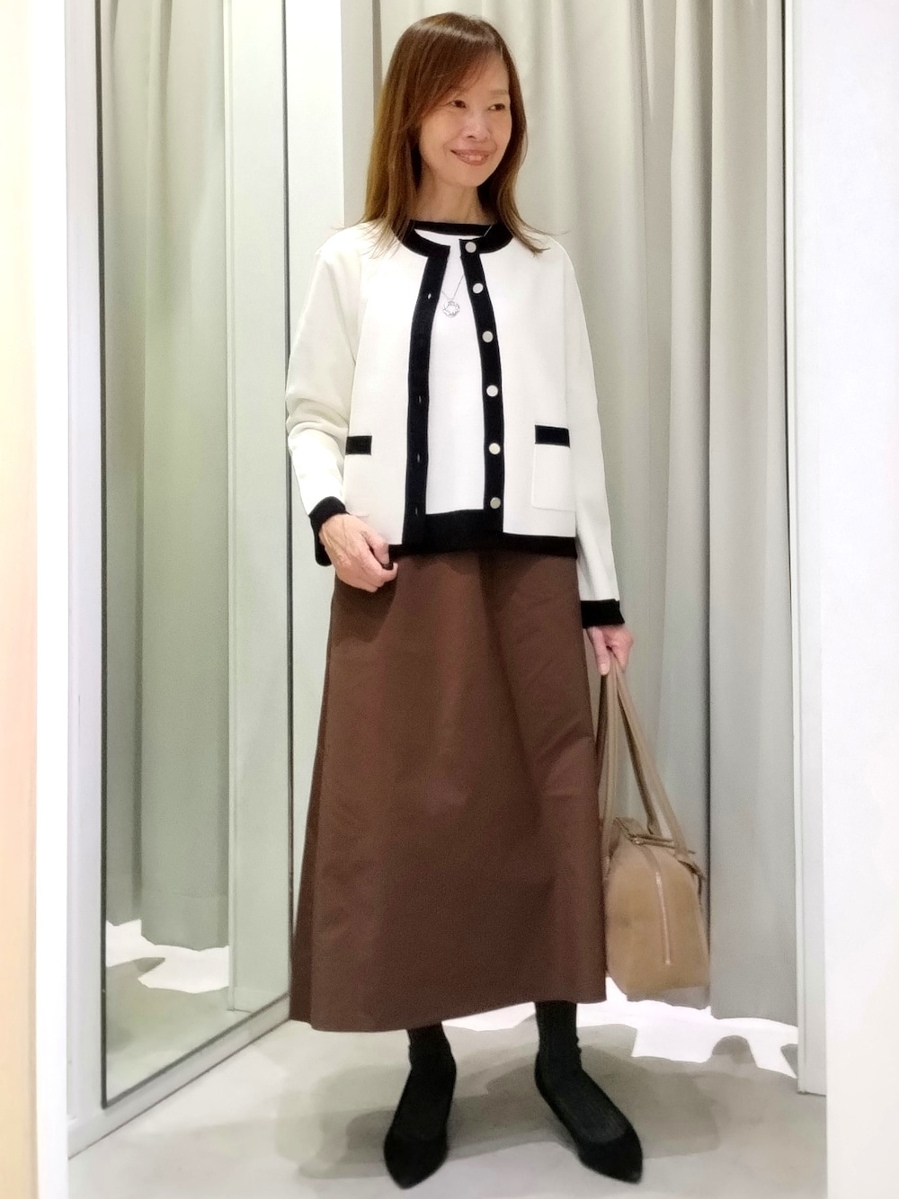 ブラウン系のスカート、ベージュ系のボストンバッグ、シルバー系のネックレスを着用したレディースの秋コーディネートの1枚目の写真