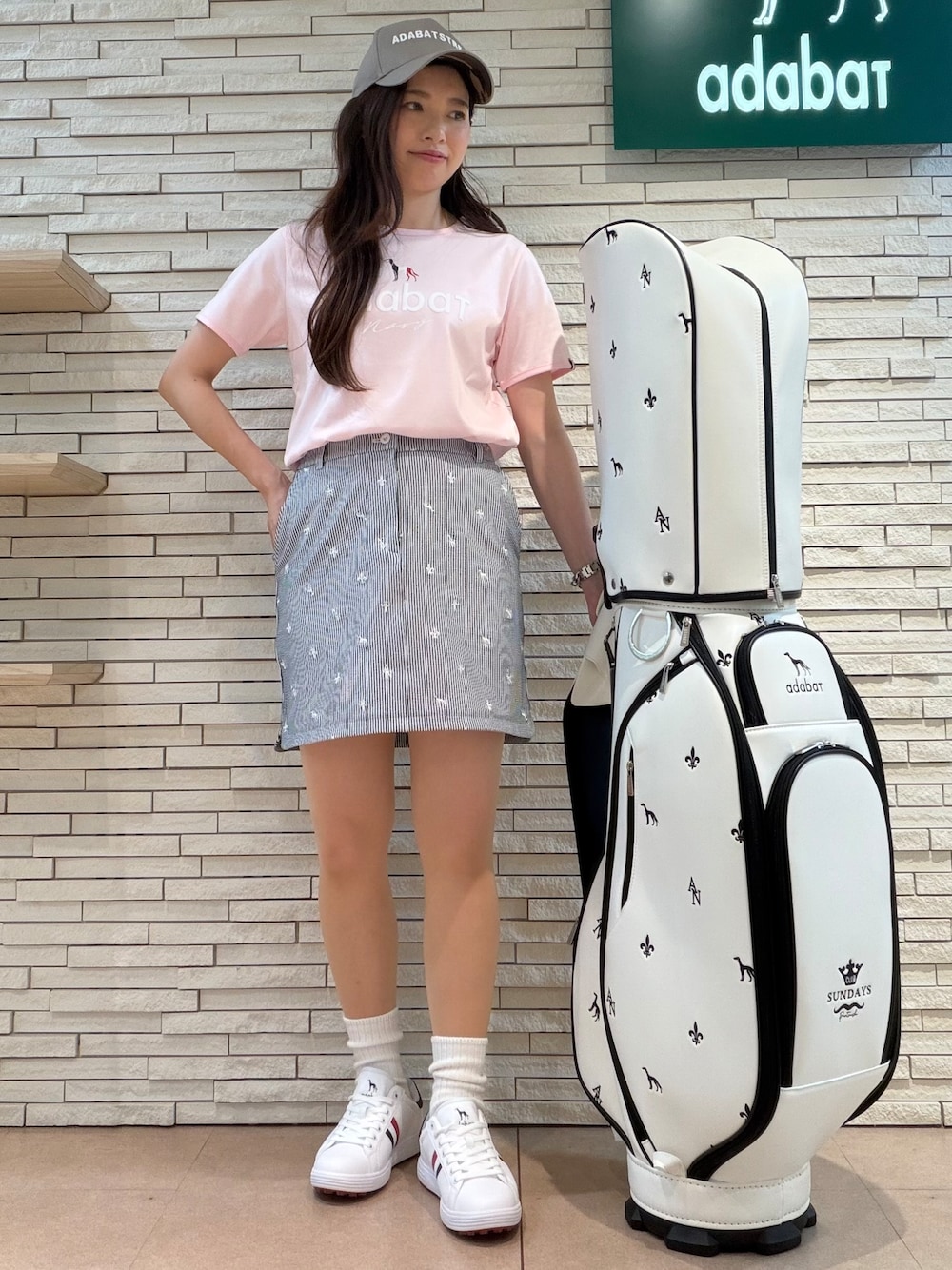 ピンク系のTシャツ/カットソー、ホワイト系のスカート、ホワイト系のゴルフグッズを着用したレディースの夏コーディネートの1枚目の写真