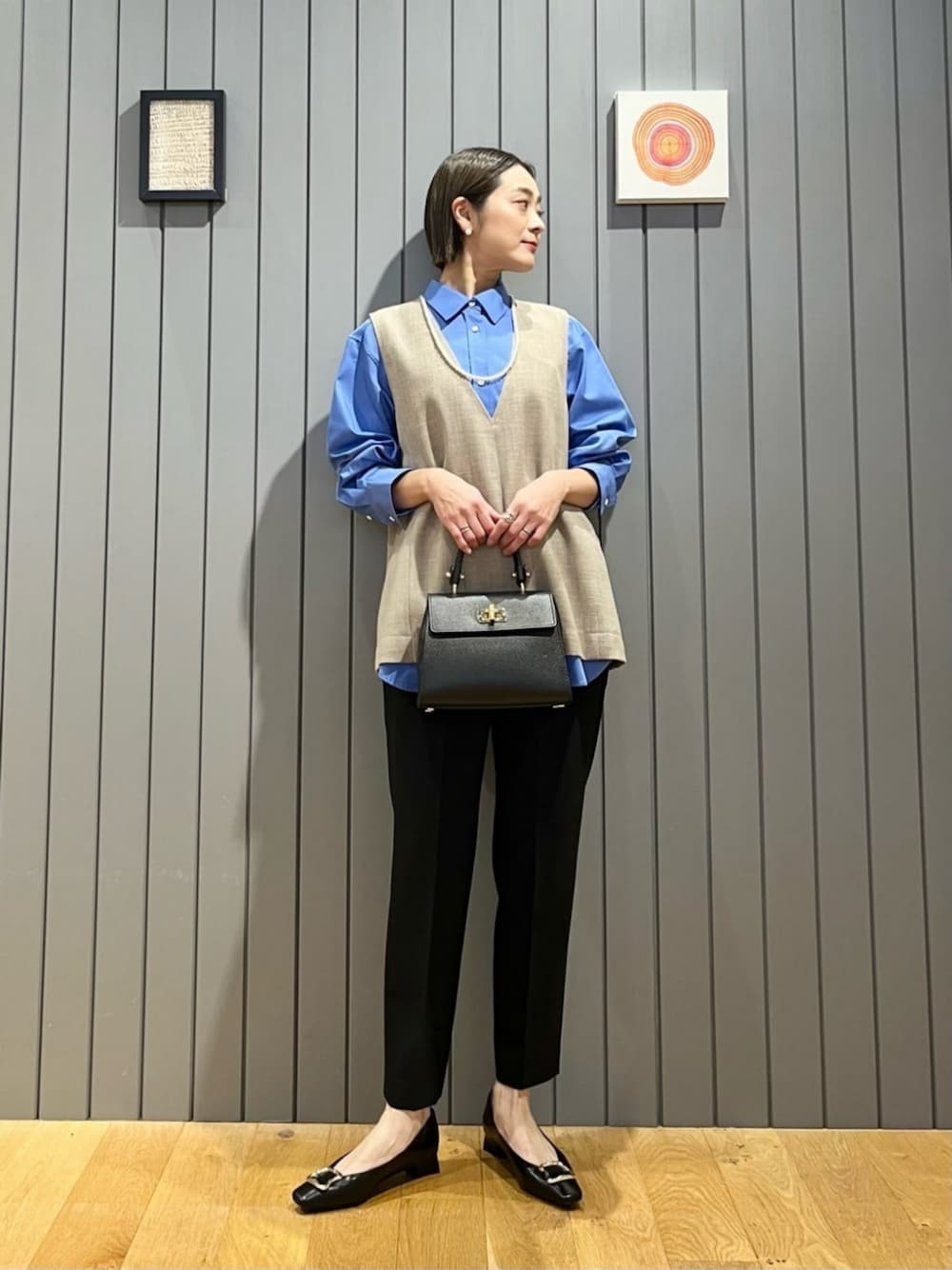 ベージュ系のベスト、ブルー系のシャツ/ブラウス、ブラック系のスラックスを着用したレディースの春コーディネートの1枚目の写真