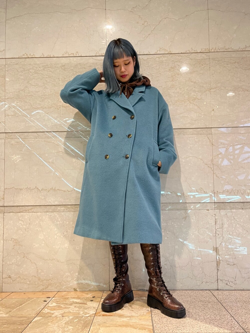 ブルー系のチェスターコート、ブラウン系のパーカー、ブラウン系のブーツを着用したレディースの冬コーディネートの1枚目の写真