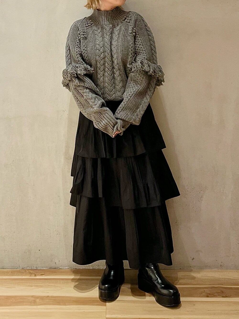 グレー系のニット/セーター、ブラック系のスカート、ブラック系のブーツを着用したレディースの秋コーディネートの1枚目の写真