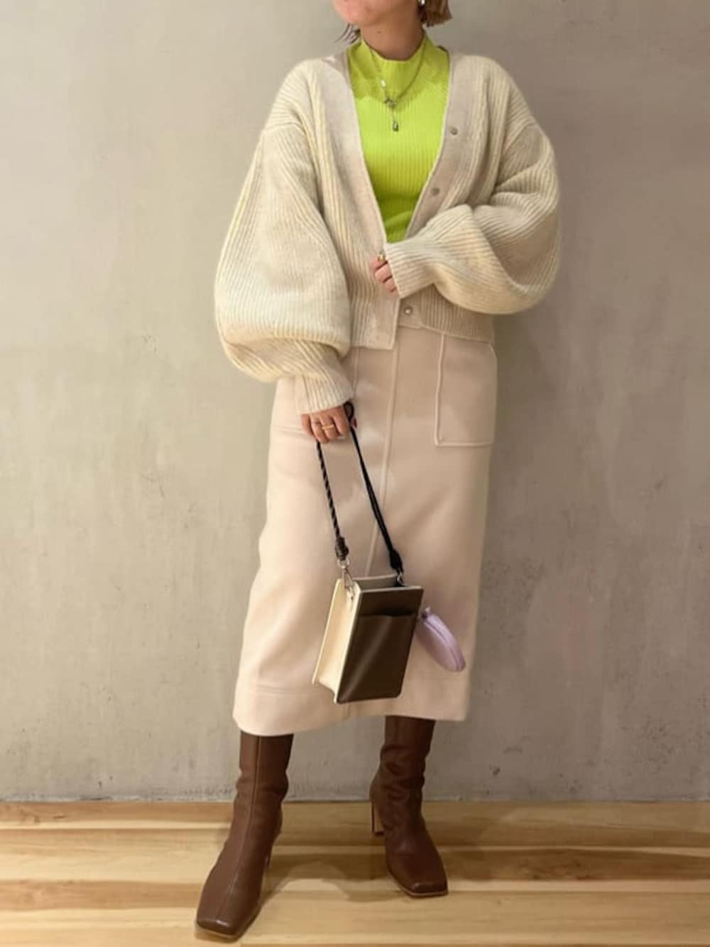 ブラウン系のブーツ、ベージュ系のショルダーバッグ、グリーン系のニット/セーターを着用したレディースの秋コーディネートの1枚目の写真