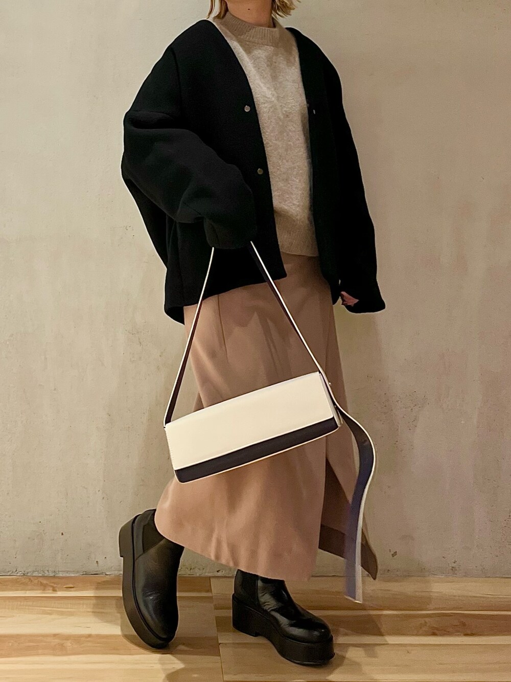 ブラック系のノーカラーコート、ベージュ系のニット/セーター、ベージュ系のスカートを着用したレディースの秋コーディネートの1枚目の写真