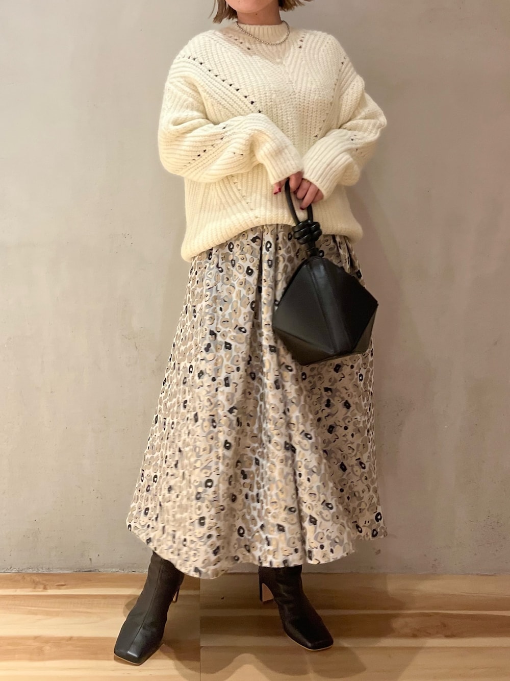 ベージュ系のスカート、ブラック系のハンドバッグ、ホワイト系のニット/セーターを着用したレディースの冬コーディネートの1枚目の写真