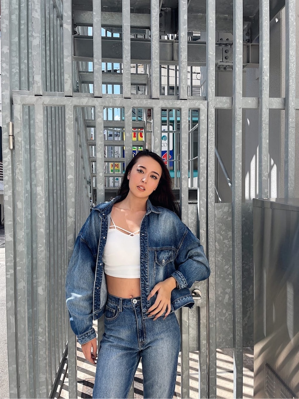 ブルー系のデニムパンツ、ブルー系のデニムジャケット、ホワイト系のキャミソールを着用したレディースの秋コーディネートの1枚目の写真