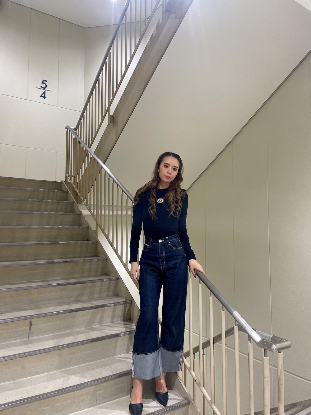 ブラック系のニット/セーター、ブルー系のデニムパンツ、ブラック系のパンプスを着用したレディースの秋コーディネートの1枚目の写真