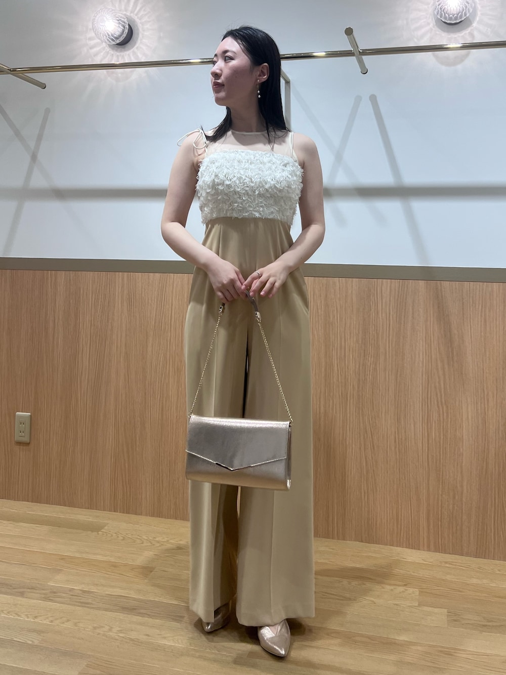 ベージュ系のパンツドレス、ゴールド系のパンプス、ゴールド系のクラッチバッグを着用したレディースの春コーディネートの1枚目の写真