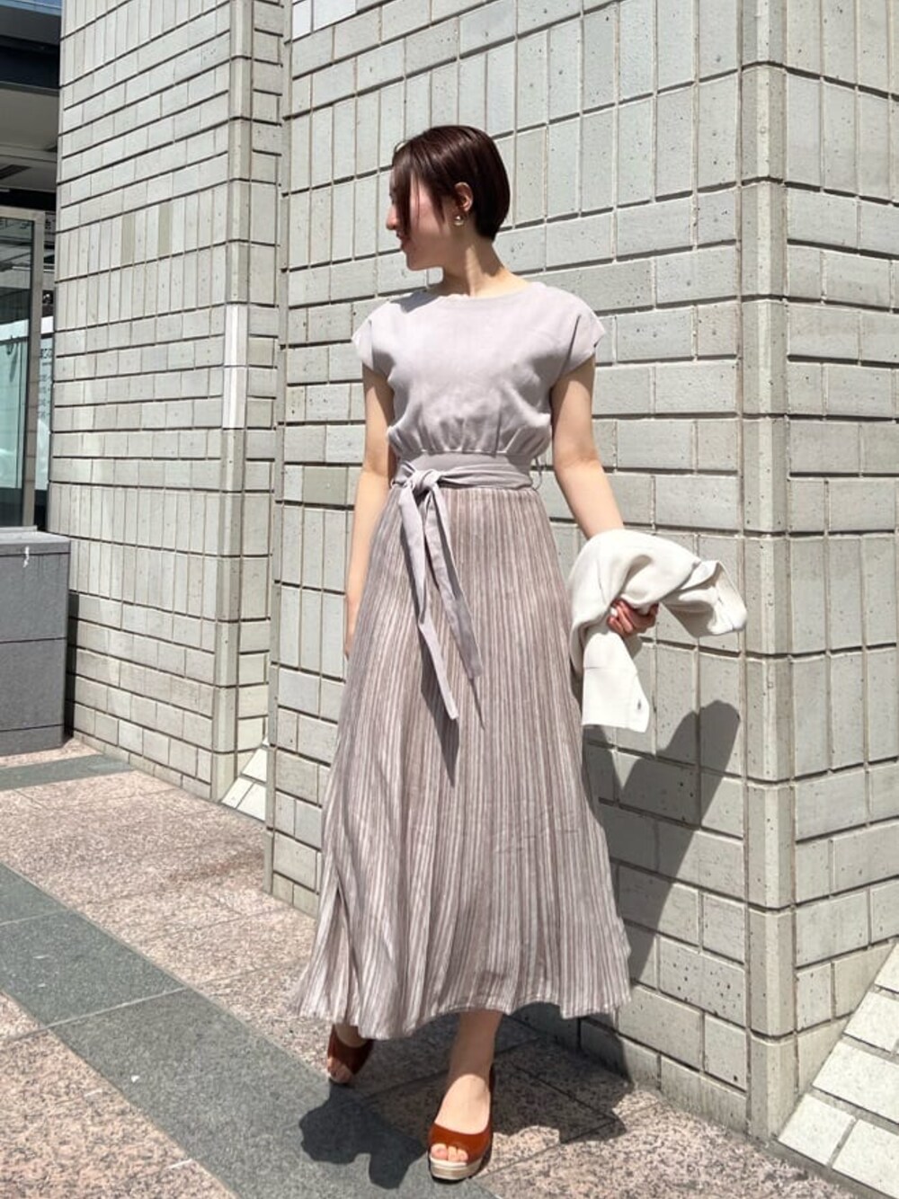 ベージュ系のワンピース、ホワイト系のカーディガン/ボレロ、ゴールド系のバングル/リストバンドを着用したレディースの春コーディネートの1枚目の写真