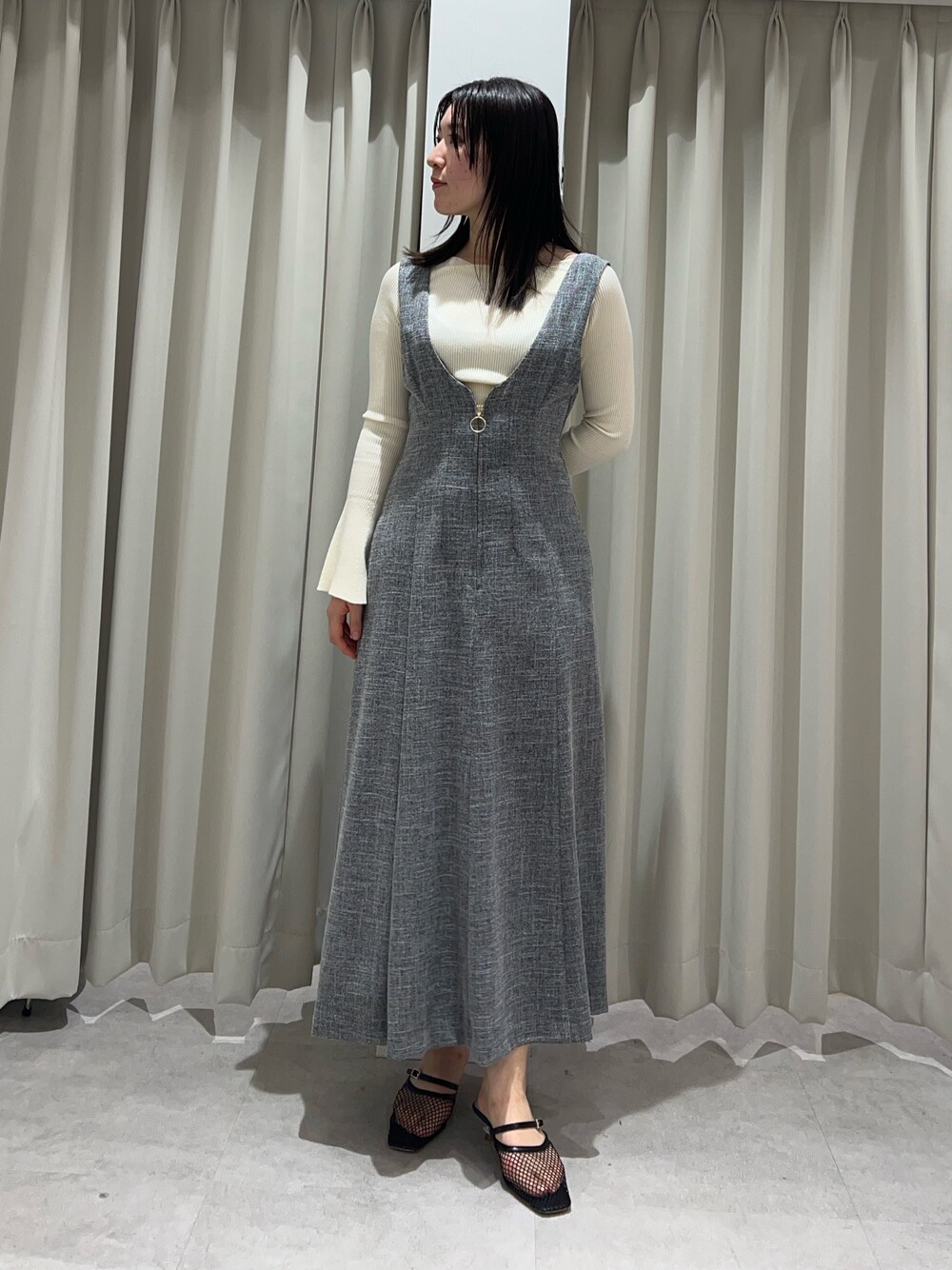 ホワイト系のニット/セーター、グレー系のジャンパースカート、ブラック系のサンダルを着用したレディースの春コーディネートの1枚目の写真
