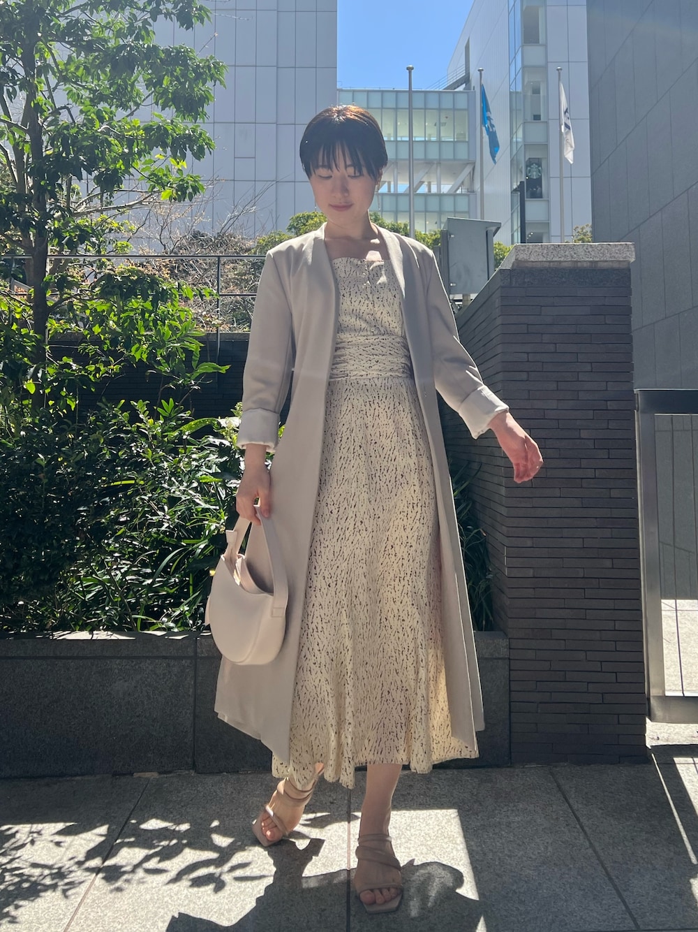 ホワイト系のハンドバッグ、ベージュ系のサンダル、ホワイト系のワンピースを着用したレディースの春コーディネートの1枚目の写真