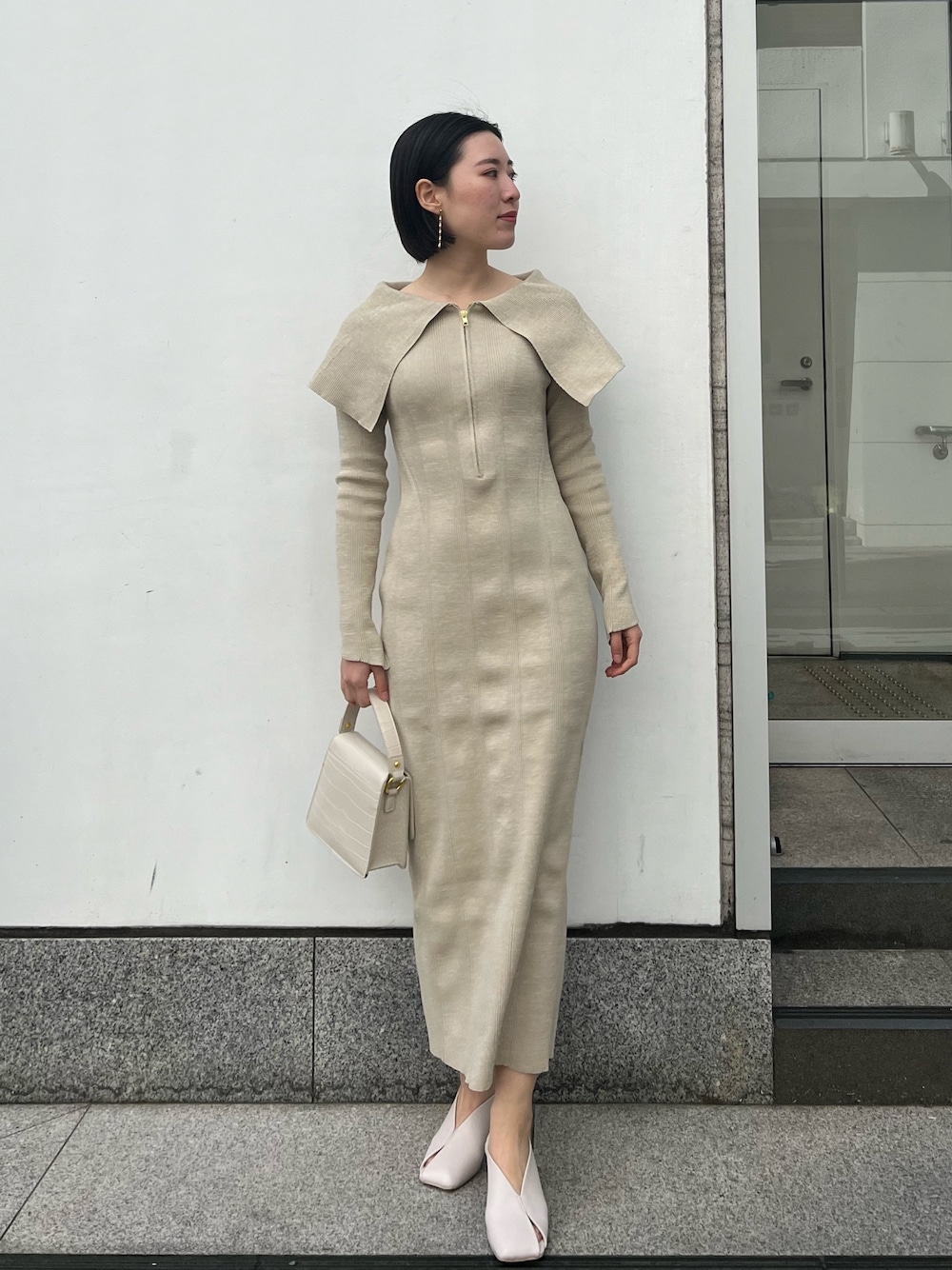 ホワイト系のパンプス、ベージュ系のワンピース、ホワイト系のショルダーバッグを着用したレディースの春コーディネートの1枚目の写真