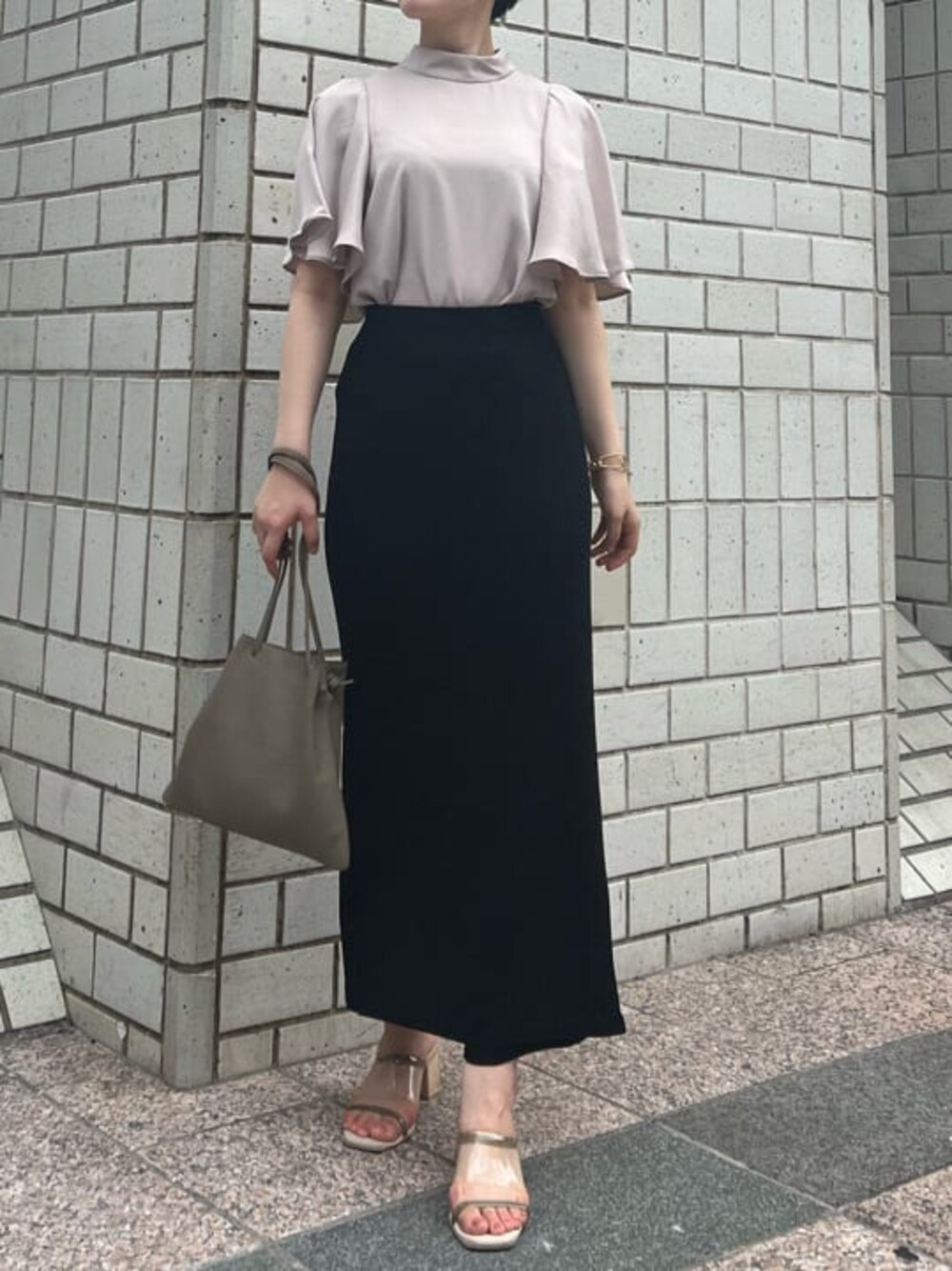 ベージュ系のハンドバッグ、グリーン系のサンダル、ブラック系のスカートを着用したレディースの夏コーディネートの1枚目の写真