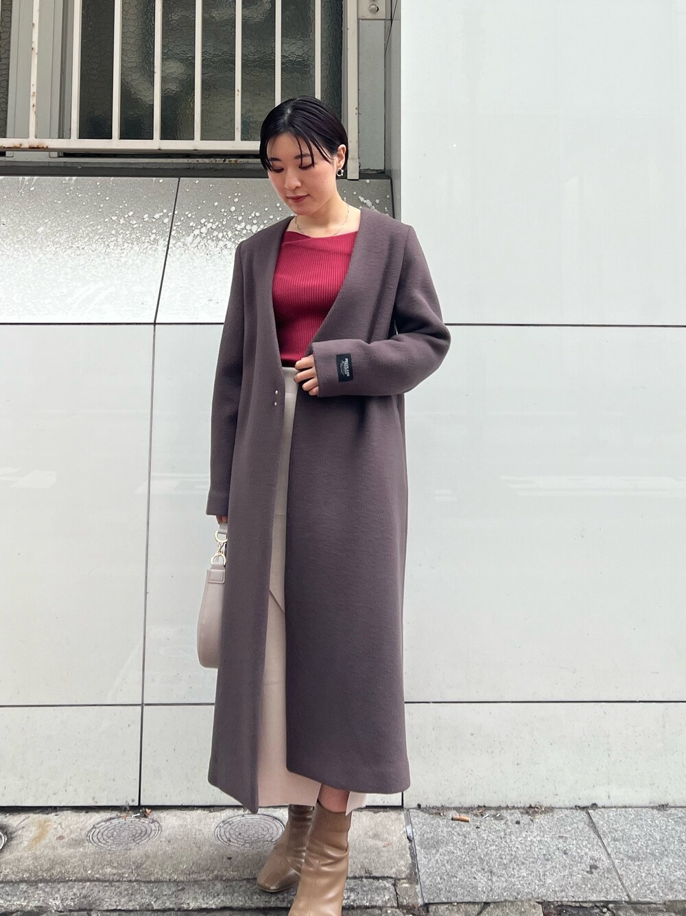 グレー系のノーカラーコート、ベージュ系のブーツ、ホワイト系のハンドバッグを着用したレディースの冬コーディネートの1枚目の写真