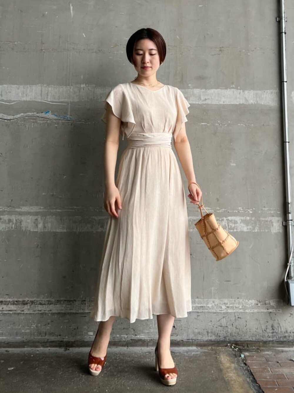 ホワイト系のワンピース、ブラウン系のパンプス、オレンジ系のショルダーバッグを着用したレディースの春コーディネートの1枚目の写真