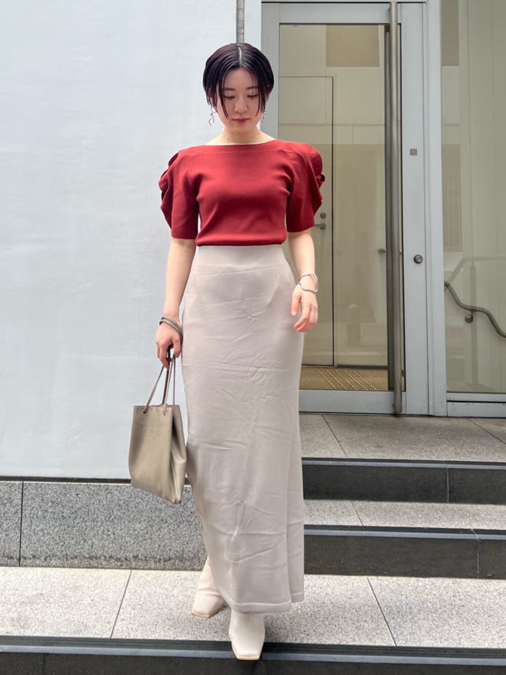 ベージュ系のハンドバッグ、ホワイト系のサンダル、ベージュ系のスカートを着用したレディースの夏コーディネートの1枚目の写真