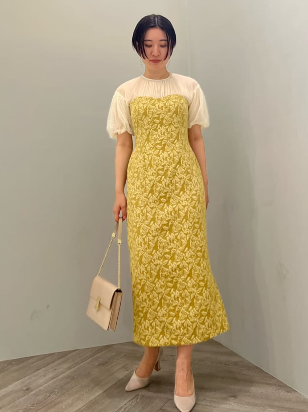 ベージュ系のパンプス、イエロー系のドレス、ベージュ系のクラッチバッグを着用したレディースの秋コーディネートの1枚目の写真