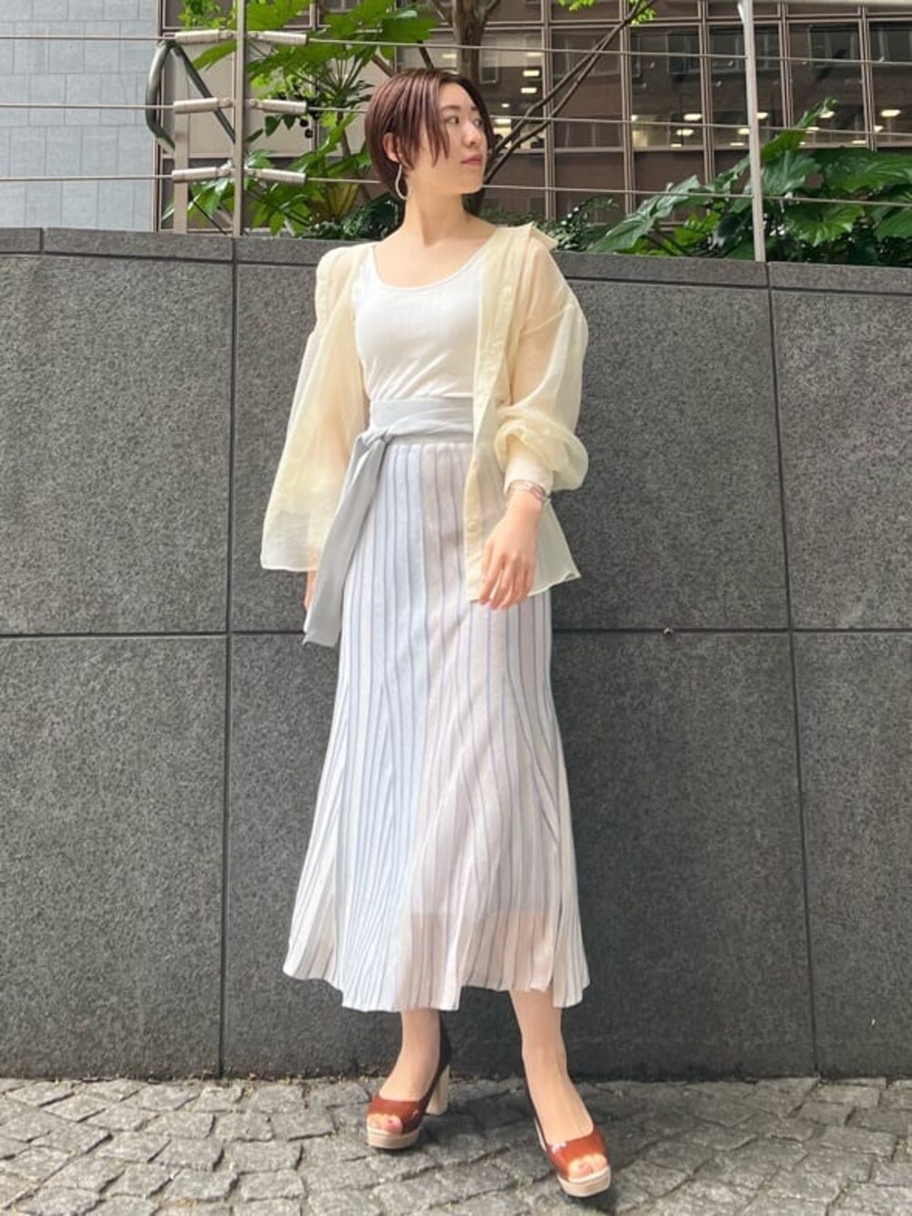 ホワイト系のシャツ/ブラウス、ブルー系のスカート、ブラウン系のパンプスを着用したレディースの春コーディネートの1枚目の写真