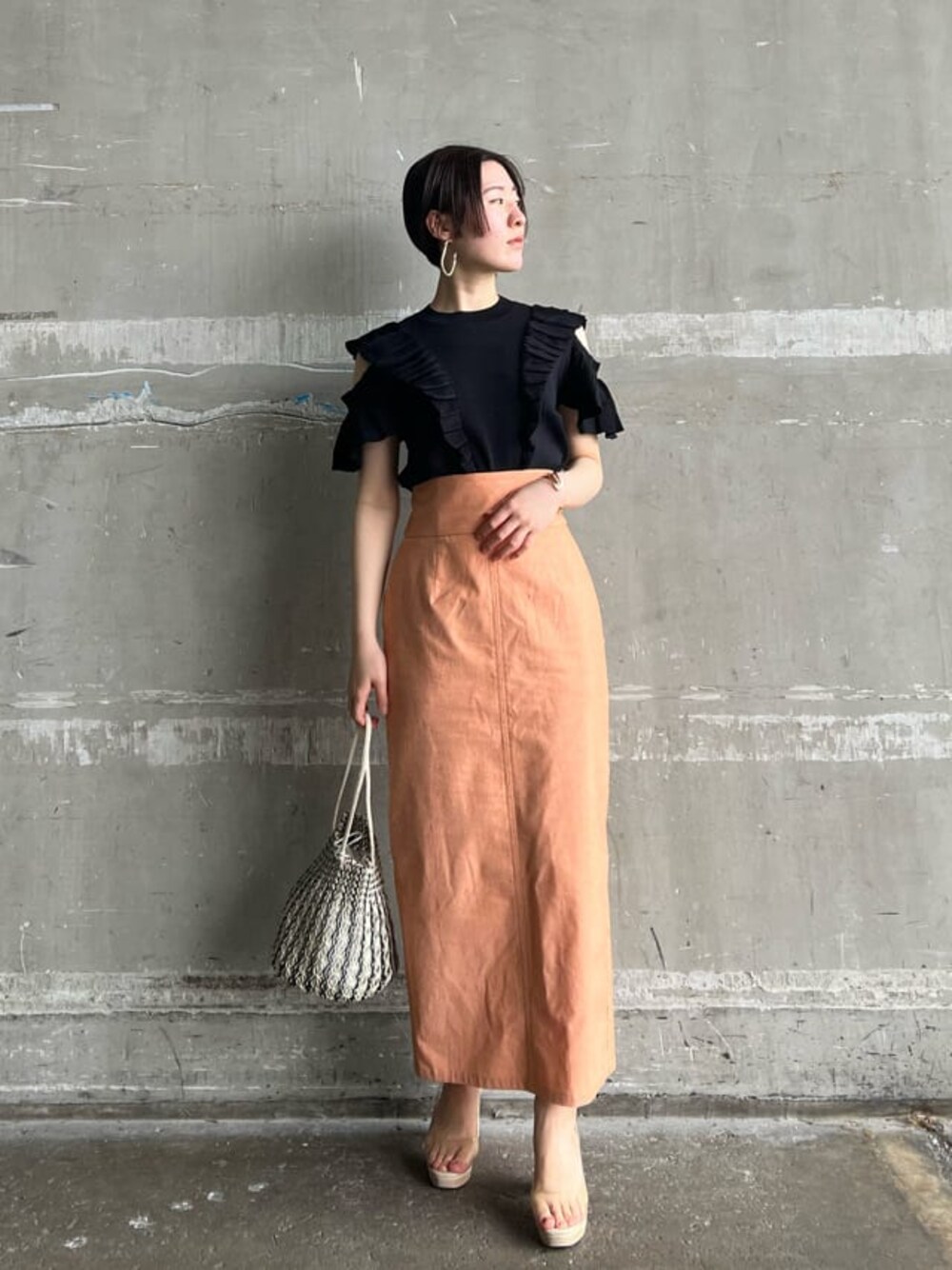 オレンジ系のスカート、その他のパンプス、ブラック系のニット/セーターを着用したレディースの春コーディネートの1枚目の写真