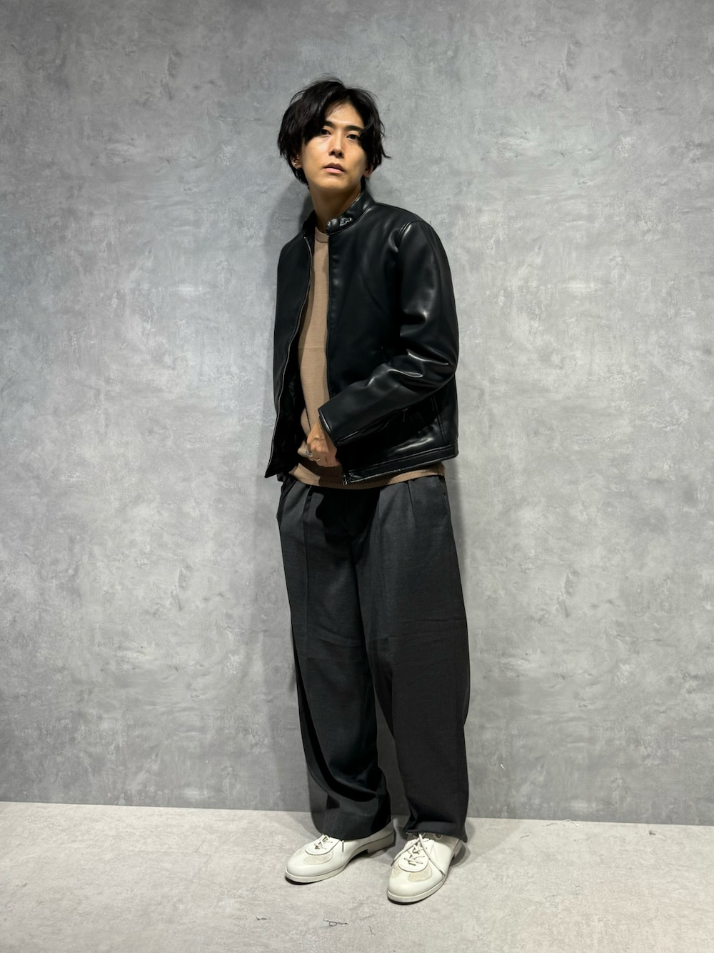 ブラック系のライダースジャケット、グレー系のスラックス、ベージュ系のニット/セーターを着用したメンズの秋コーディネートの1枚目の写真