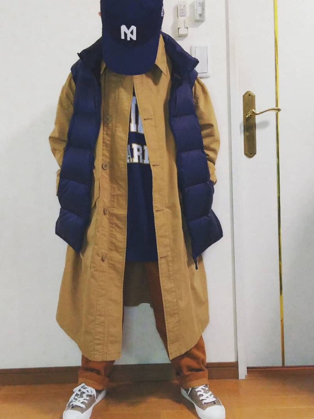 ブルー系のダウンベスト、ベージュ系のステンカラーコート、ブラウン系のその他パンツを着用したレディースの秋コーディネートの1枚目の写真