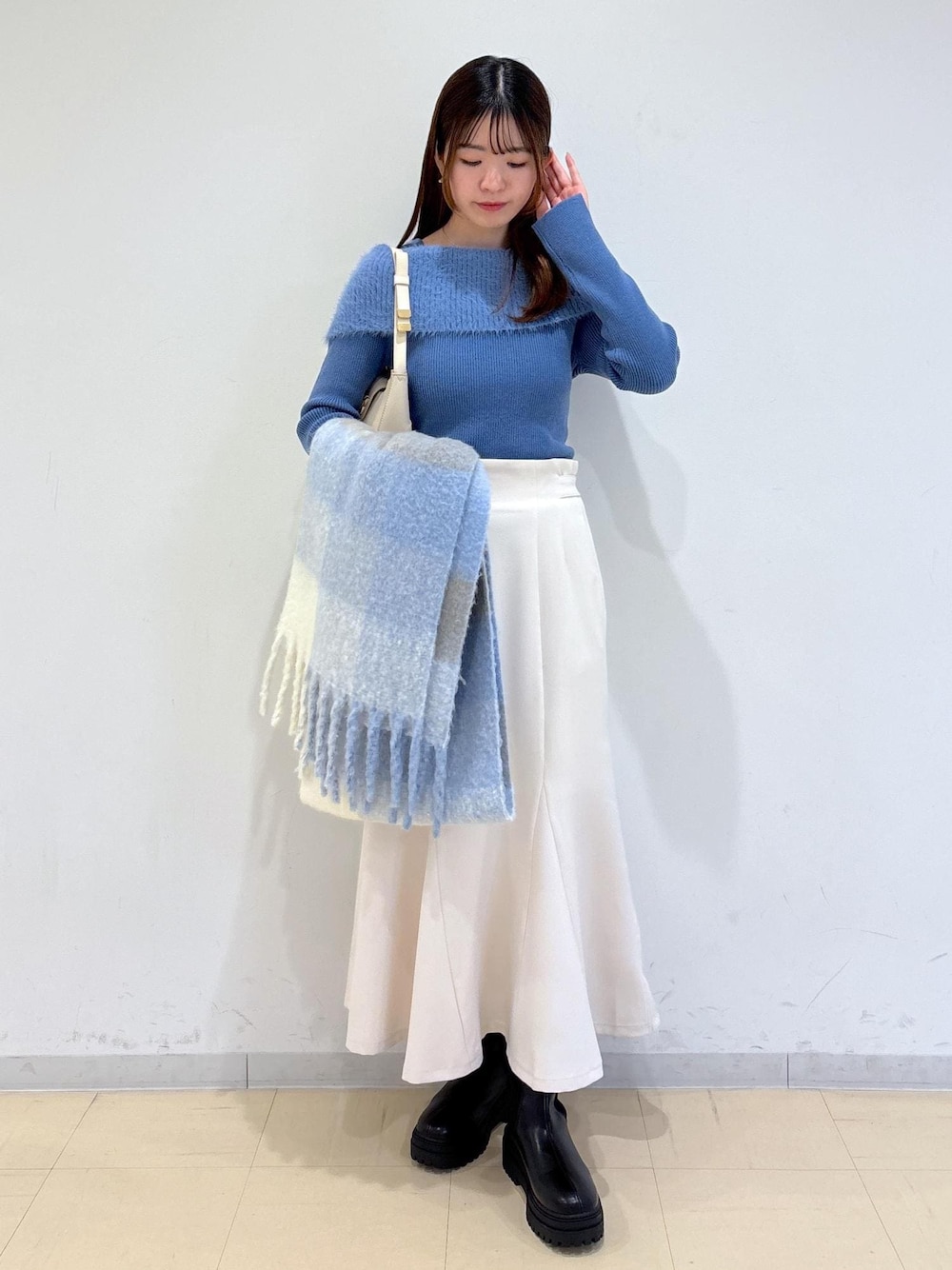 ホワイト系のショルダーバッグ、ブラック系のブーツ、ブルー系のニット/セーターを着用したレディースの秋コーディネートの1枚目の写真