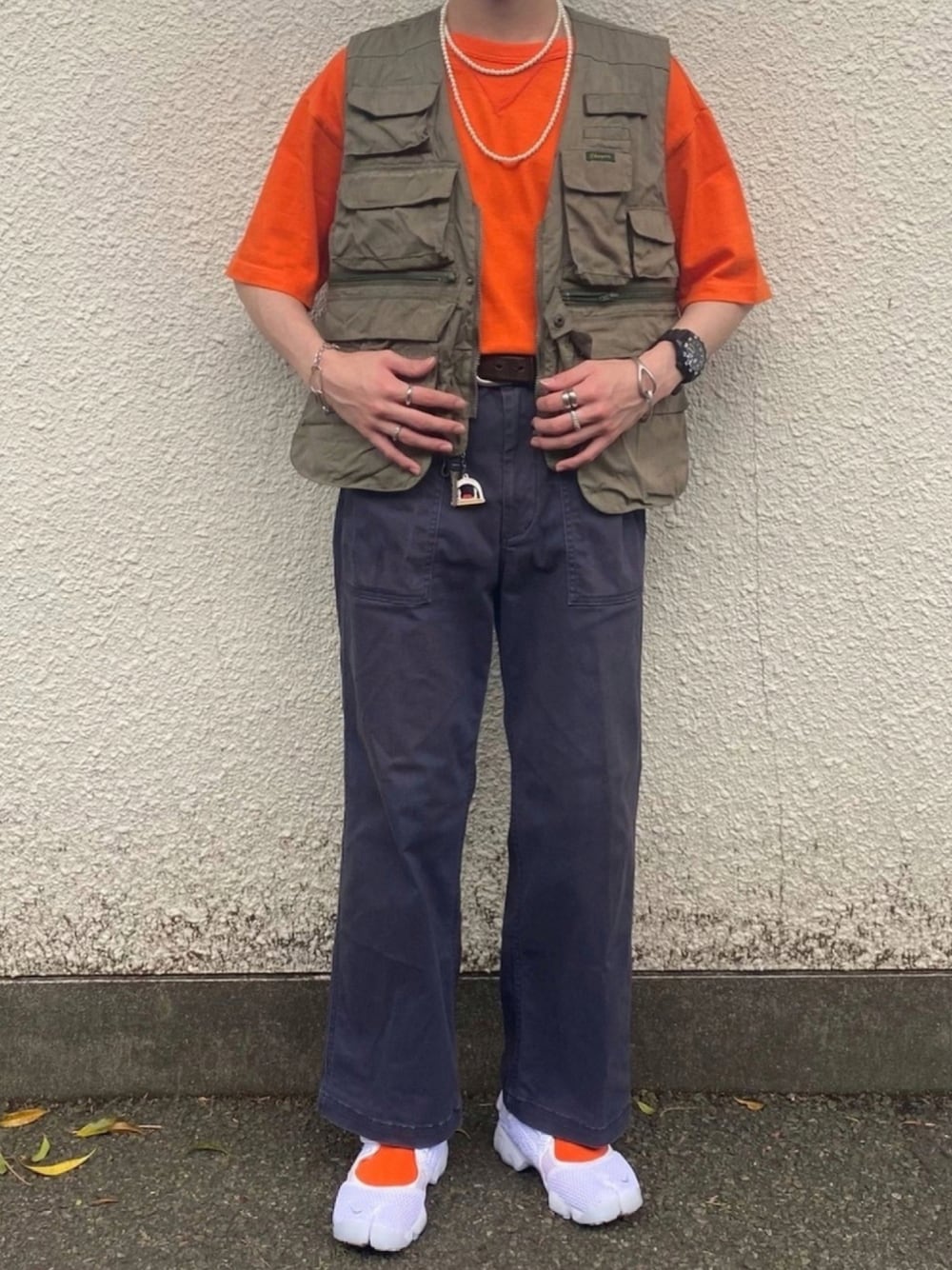 ブラック系のパンツ、グリーン系のベスト、オレンジ系のTシャツ/カットソーを着用したメンズの夏コーディネートの1枚目の写真