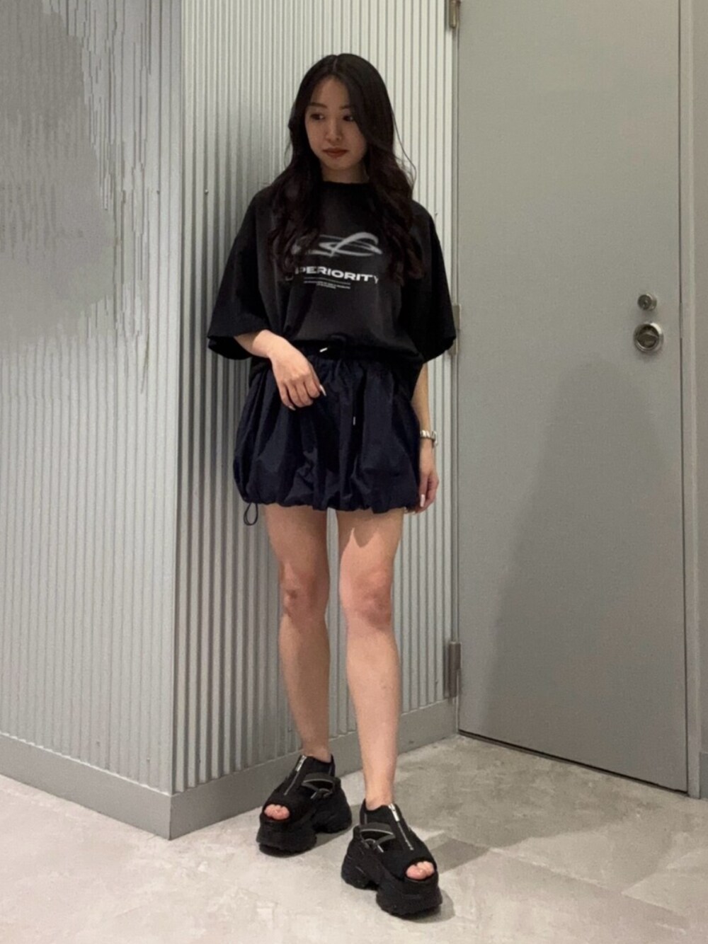 ブラック系のTシャツ/カットソー、ブルー系のスカート、ブラック系のサンダルを着用したレディースの春コーディネートの1枚目の写真