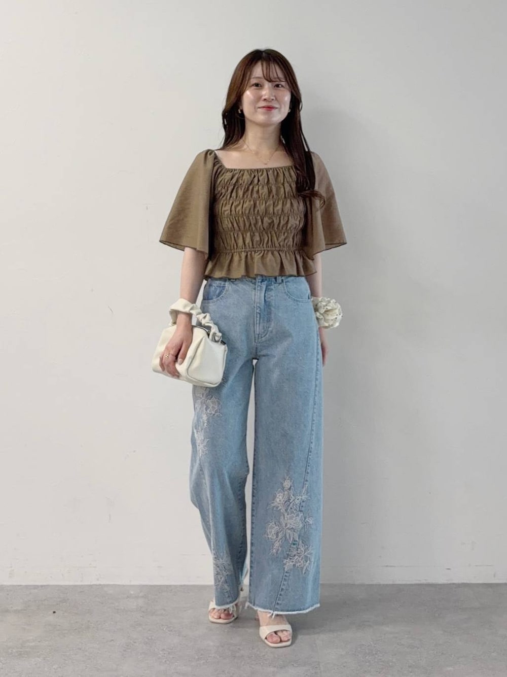 ブラウン系のワンピース、ブルー系のデニムパンツ、ホワイト系のサンダルを着用したレディースの秋コーディネートの1枚目の写真