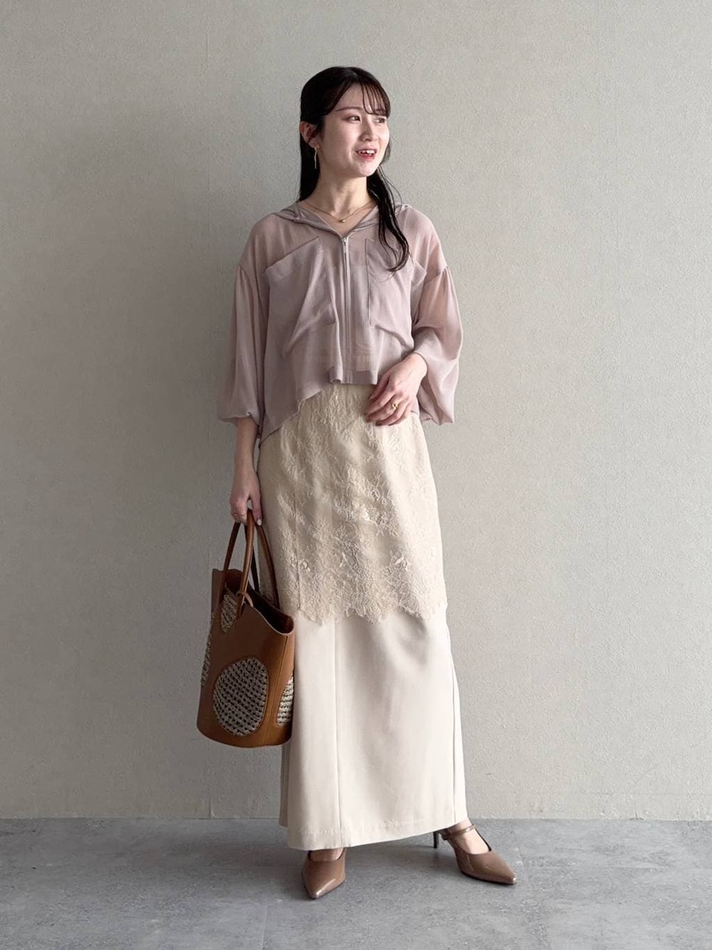 ベージュ系のパーカー、ブラウン系のトートバッグ、ベージュ系のスカートを着用したレディースの春コーディネートの1枚目の写真