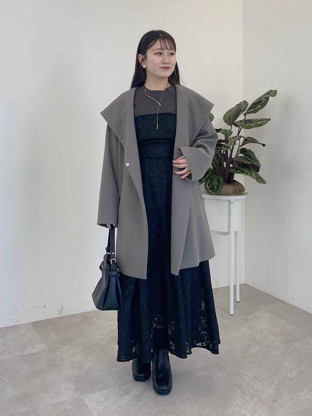 グレー系のノーカラーコート、ブラック系のショルダーバッグ、ブラック系のブーツを着用したレディースの冬コーディネートの1枚目の写真