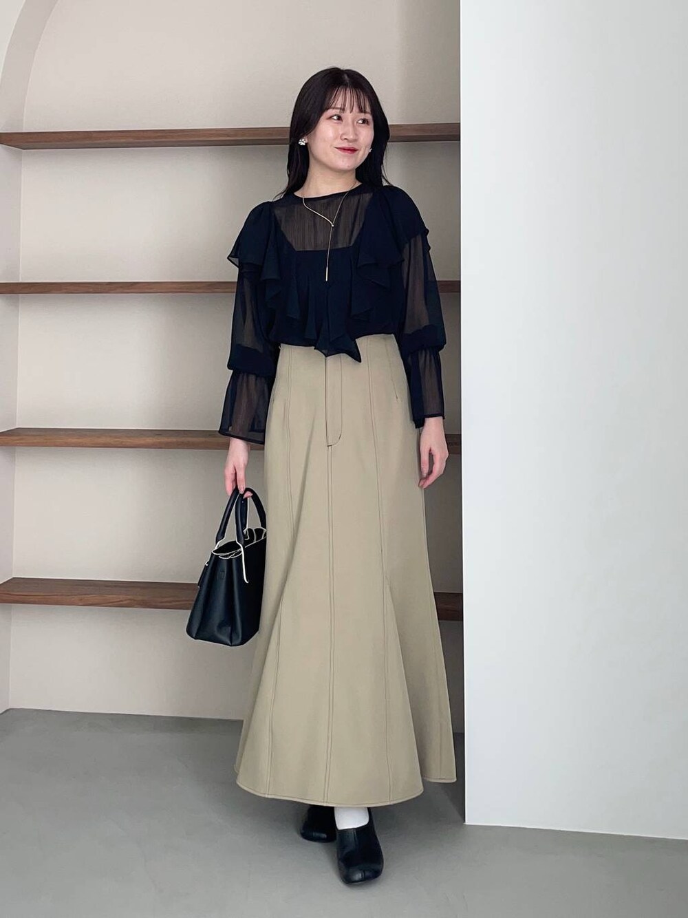 ブラック系のショルダーバッグ、ブラック系のパンプス、ベージュ系のスカートを着用したレディースの春コーディネートの1枚目の写真