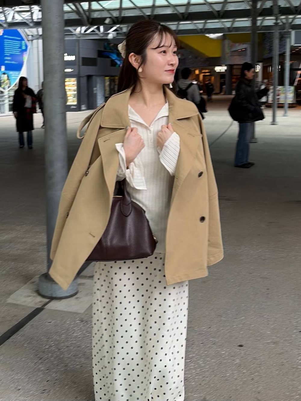 ホワイト系のスカート、ブラウン系のボストンバッグ、ベージュ系のトレンチコートを着用したレディースの冬コーディネートの1枚目の写真