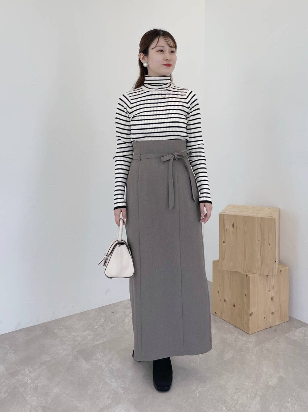 ブラウン系のスカート、ホワイト系のハンドバッグ、ブラック系のブーツを着用したレディースの秋コーディネートの1枚目の写真