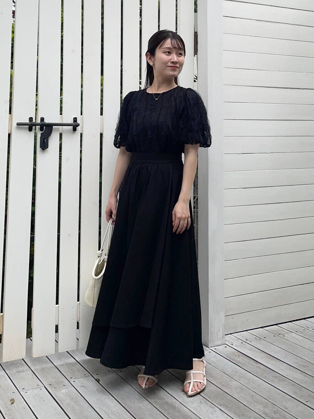 ホワイト系のハンドバッグ、ホワイト系のサンダル、ブラック系のシャツ/ブラウスを着用したレディースの夏コーディネートの1枚目の写真