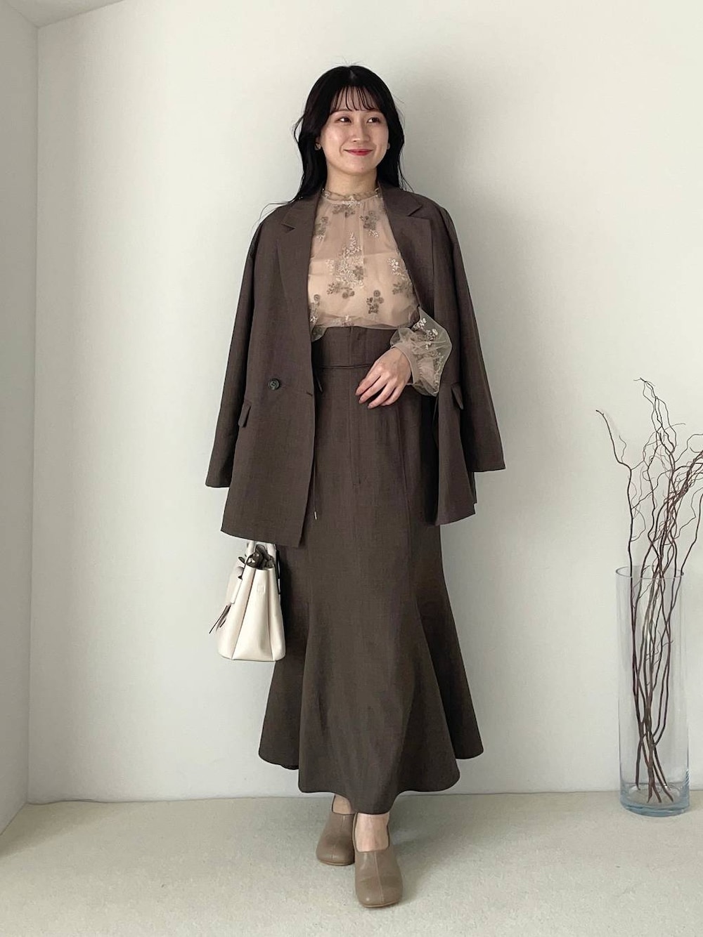 ホワイト系のショルダーバッグ、ブラウン系のパンプス、グレー系のスカートを着用したレディースの春コーディネートの1枚目の写真