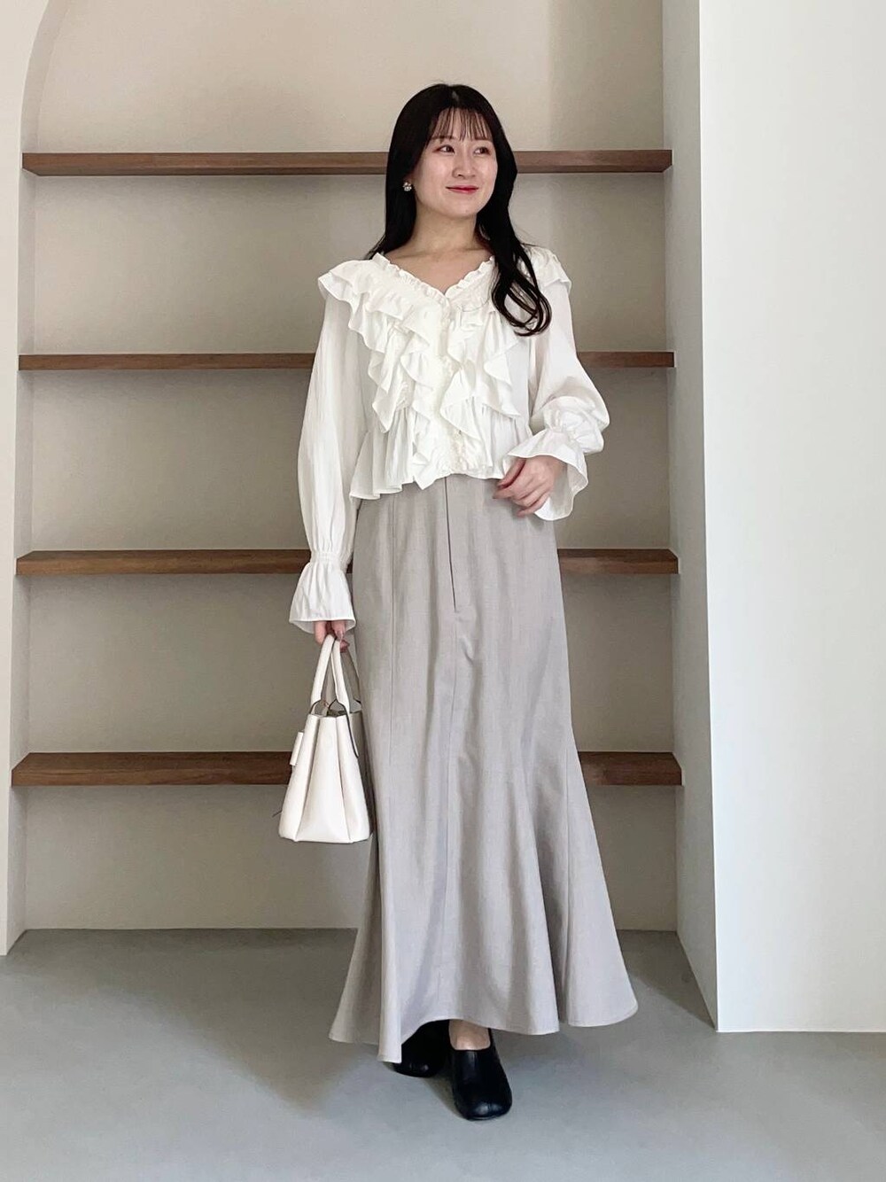 ホワイト系のショルダーバッグ、ホワイト系のシャツ/ブラウス、ブラック系のパンプスを着用したレディースの冬コーディネートの1枚目の写真