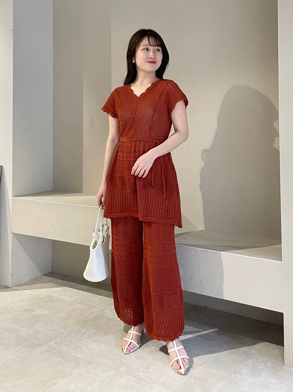 ホワイト系のハンドバッグ、オレンジ系のニット/セーター、ホワイト系のサンダルを着用したレディースの春コーディネートの1枚目の写真