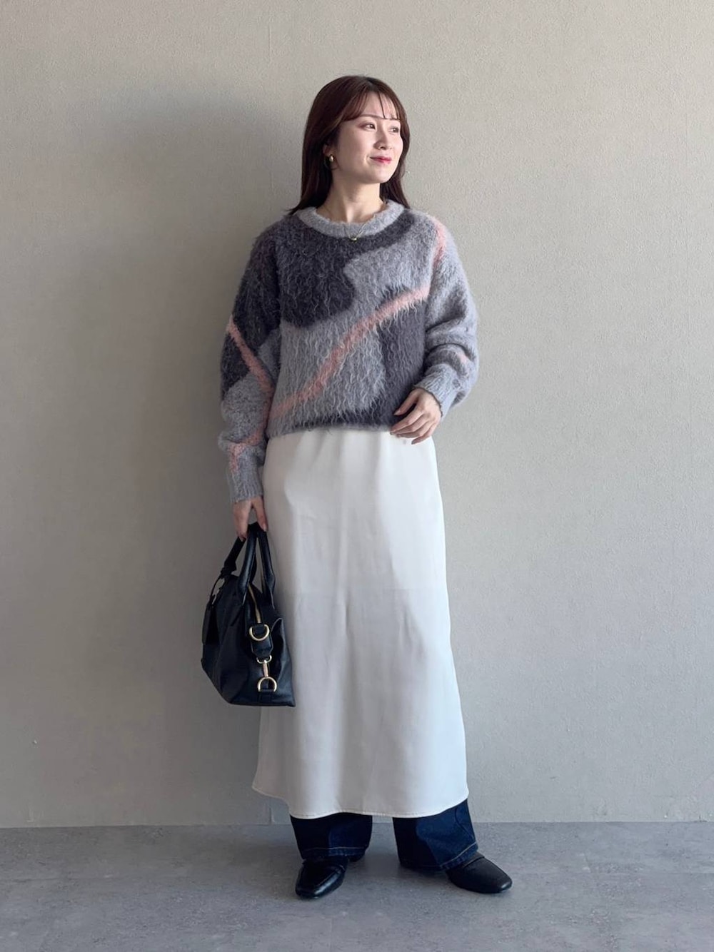 グレー系のニット/セーター、ブラック系のボストンバッグ、ブルー系のデニムパンツを着用したレディースの冬コーディネートの1枚目の写真